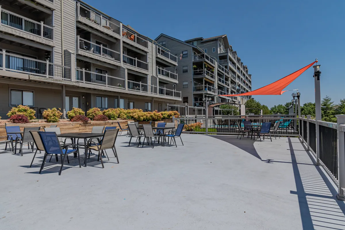 A sun-drenched outdoor seating area features colorful umbrellas, flower beds, and ample space for social gatherings. The scene is vibrant and inviting, signaling opportunities for summer barbecues, morning coffee, or relaxed evenings outdoors with family and friends.