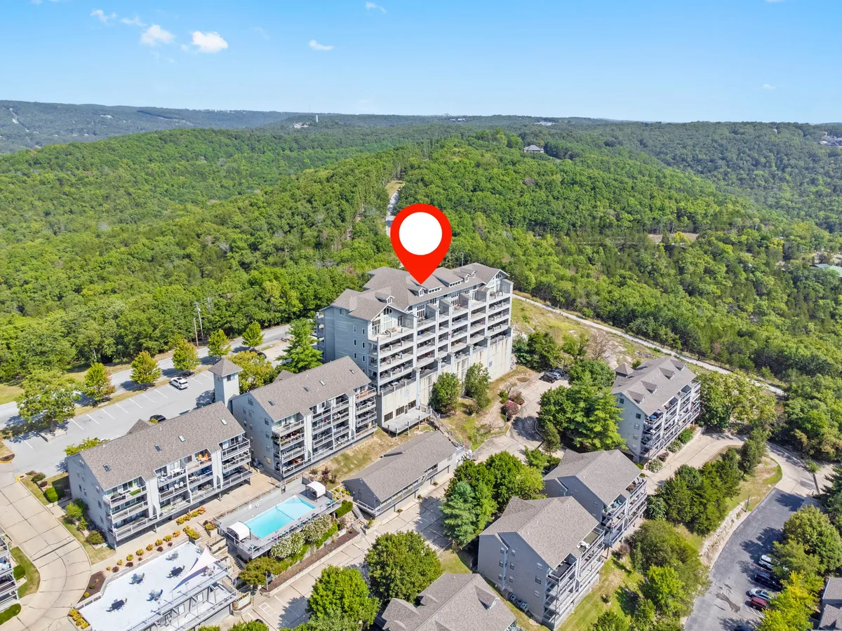 A wide exterior view of the multi-story condominium building with a swimming pool, landscaped grounds, and a convenient parking area. The setting is peaceful with mountain views and plenty of space for boat or trailer parking.