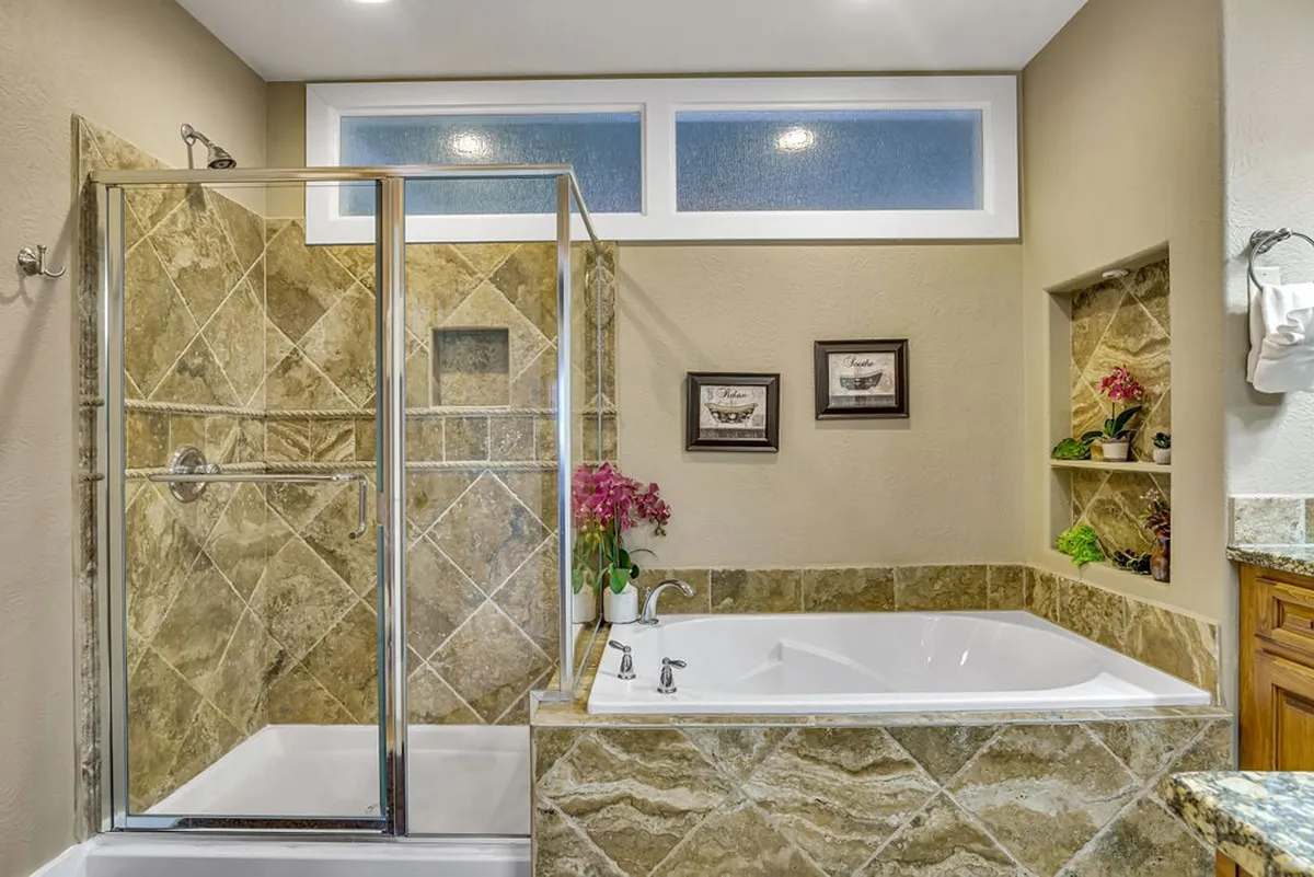 A luxurious bathroom scene featuring a glass-enclosed shower, a jacuzzi soaking tub, decorative plants, and framed artwork. The spa-like ambiance is reinforced by soft lighting and elegant fixtures.