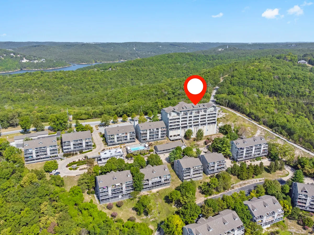 A sweeping exterior shot of the resort showcases residential buildings set amid lush greenery, with an inviting swimming pool area in the foreground and a scenic mountainous landscape beyond. The view captures the harmony between nature and the resort's recreational amenities, suggesting both relaxation and outdoor adventure.