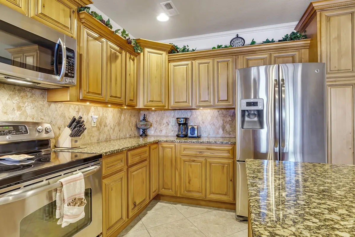A warm and inviting kitchen space with premium stainless steel appliances, granite countertops, wood cabinetry, and subtle decorative touches like potted plants. Sunlight streams in, suggesting a bright start to any day spent cooking or sharing meals with family.