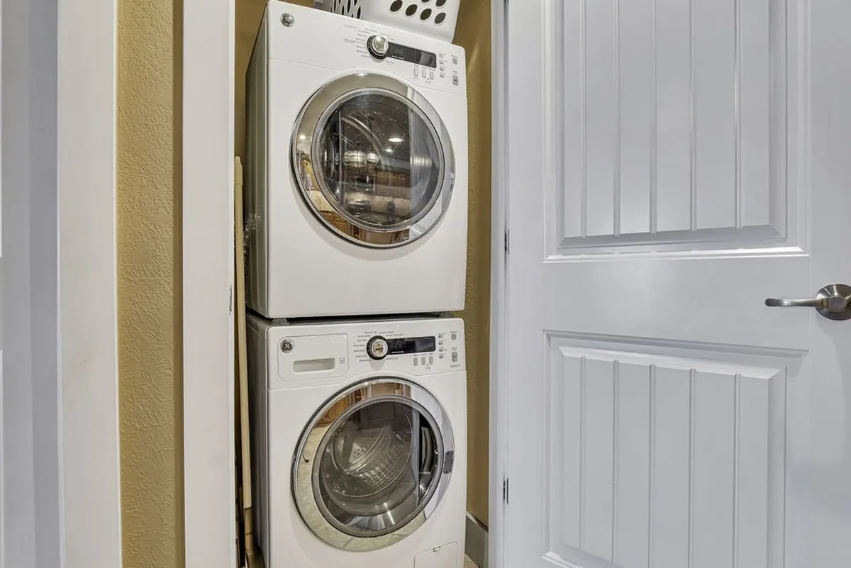 A bright and functional laundry area featuring a stacked washer and dryer with a laundry basket nearby. The compact setup is located in the hallway, offering convenient access for daily or extended stays.