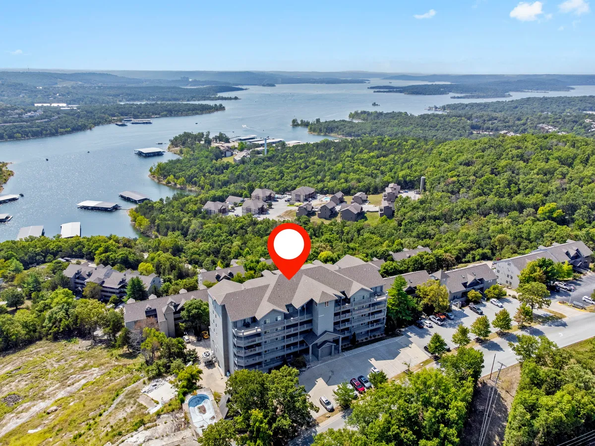 This image features a tranquil lakeside scene with a multi-story building nestled amid lush greenery, looking out over the calm waters of the lake. The view captures the serene atmosphere, with hints of recreational activities like boating and nature walks visible in the surroundings. The sunset creates a warm and inviting glow over the landscape, highlighting the peaceful ambiance.