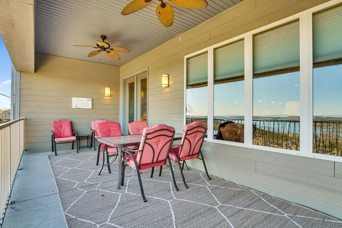 An outdoor balcony space furnished with patio chairs and a table, overlooking scenic views from an elevated position. The area is set up for relaxation, outdoor dining, or simply enjoying quiet moments, with ceiling fans providing extra comfort. The ambiance suggests both social gatherings and private moments, especially at sunset.