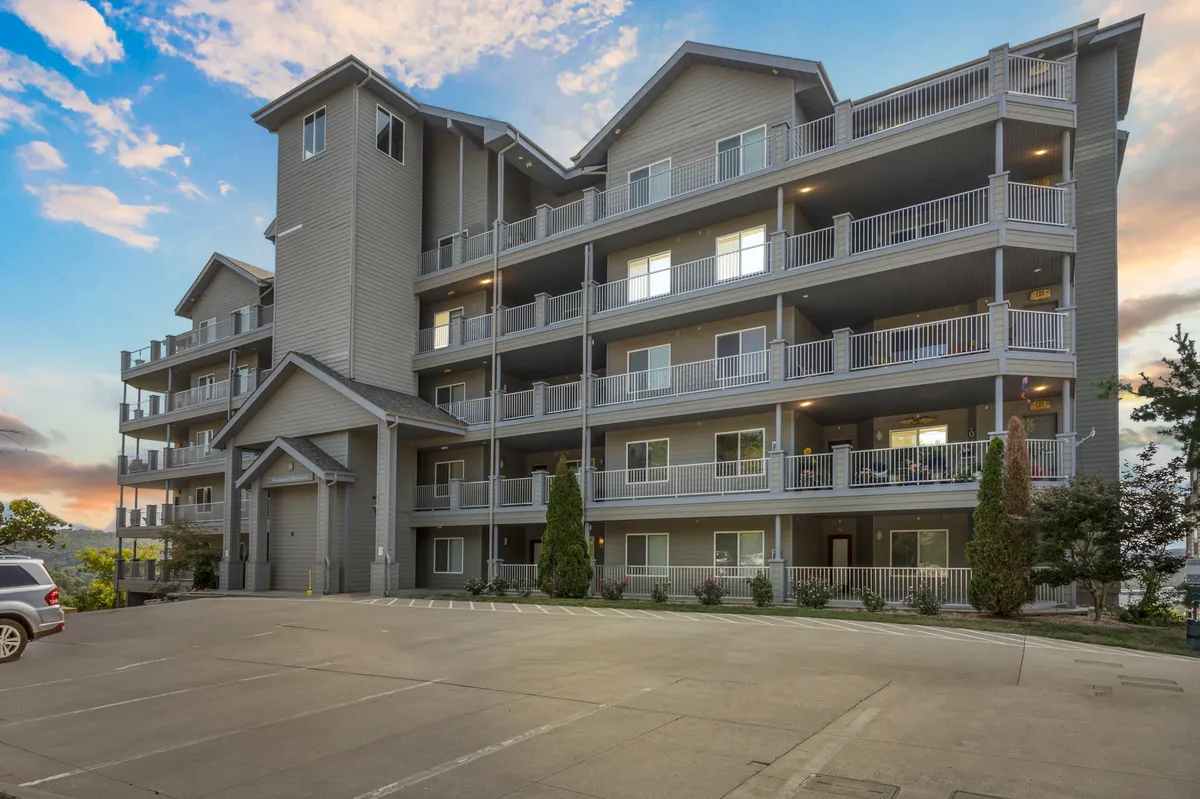 A multi-story condo building with inviting balconies and lush landscaping, captured at sunset. Residents can be seen relaxing on balconies and socializing in the courtyard below, giving the property a lively, communal feel. The building is accessible, with visible walkways and a welcoming environment.