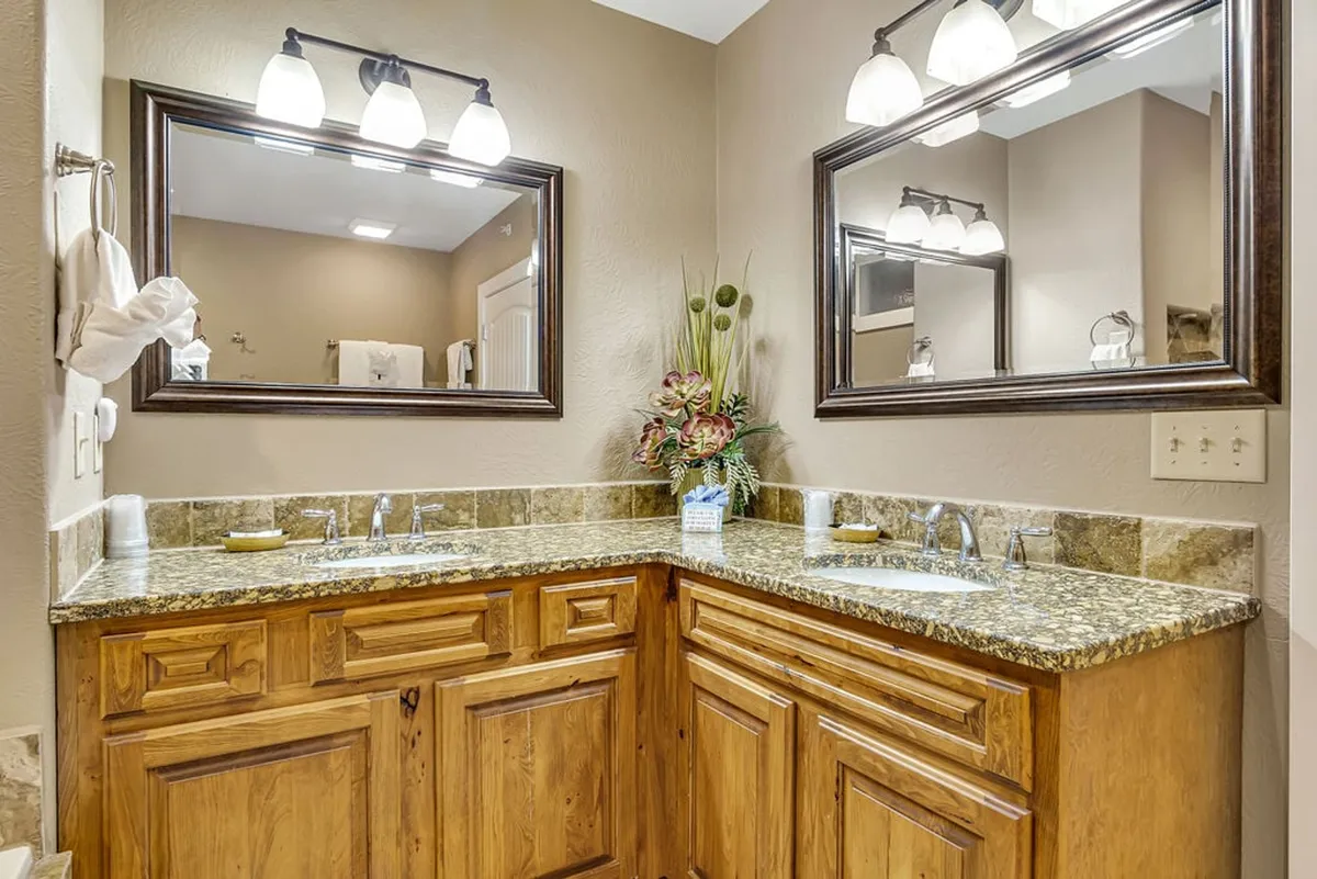 A spacious and modern bathroom showcasing a double sink vanity, wide mirrors, and a decorative plant arrangement. The clean lines and organized layout create a calm, functional space.